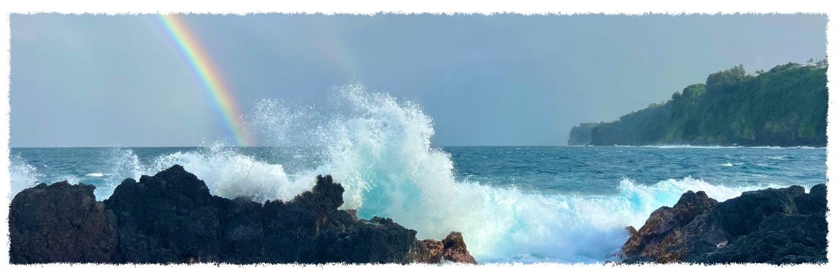Waves crashing against volcanic rock at Laupāhoehoe Point with a rainbow over the Hāmākua Coast, Big Island of Hawaiʻi.