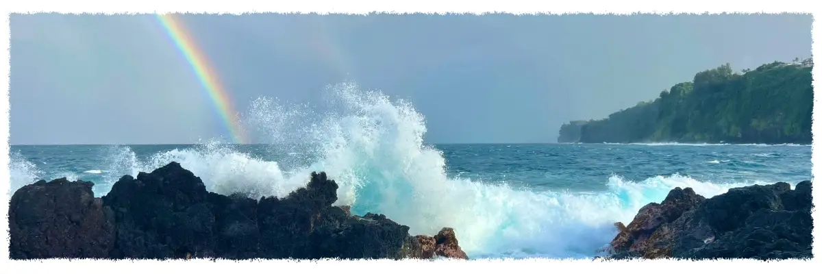 Waves crashing against volcanic rock at Laupāhoehoe Point with a rainbow over the Hāmākua Coast, Big Island of Hawaiʻi.