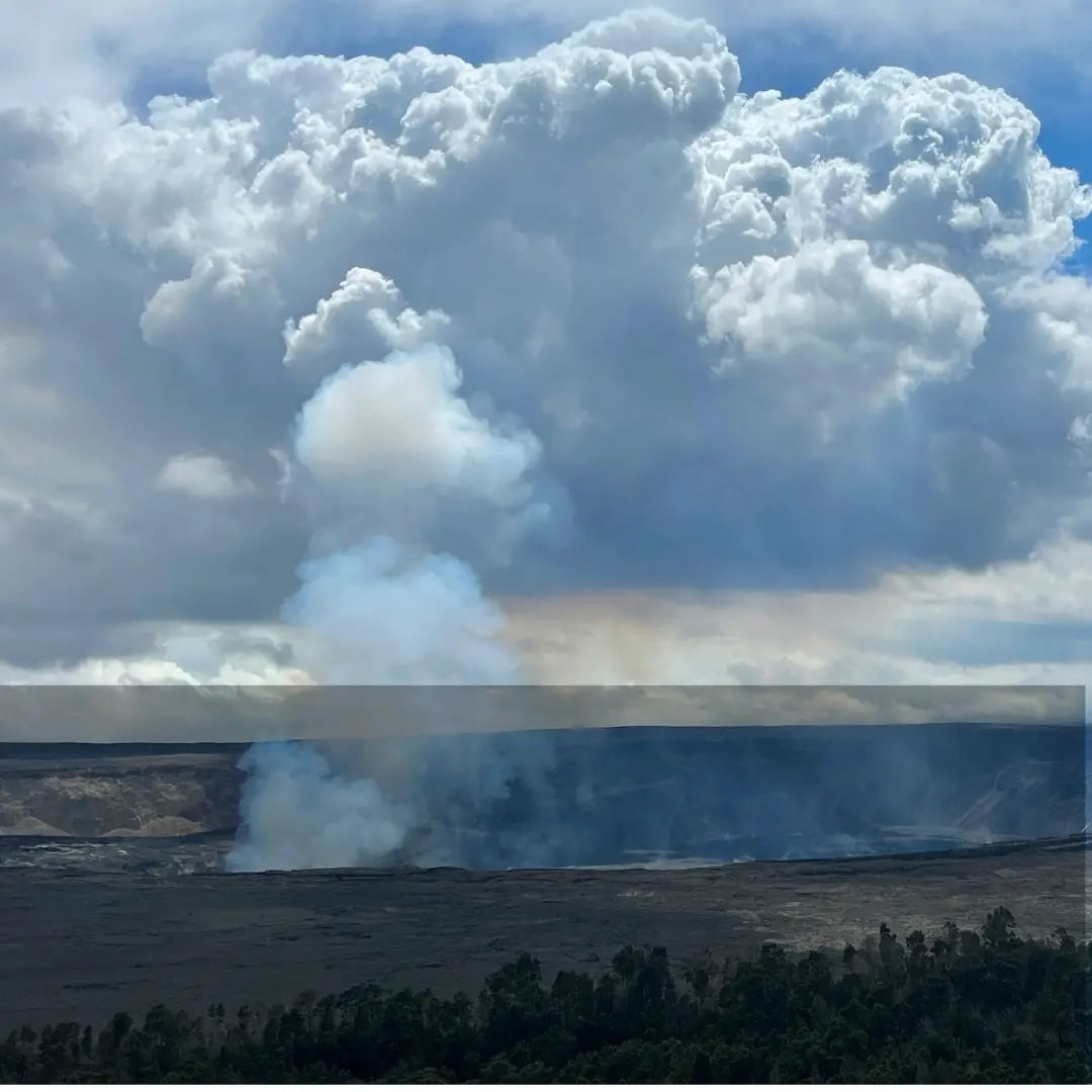 Kīlauea Caldera in Hawaiʻi Volcanoes National Park, with steam vents rising from the crater floor beneath towering clouds.
